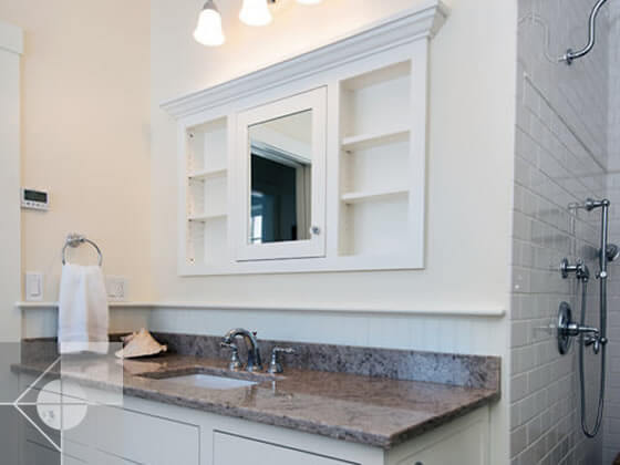 Bathroom sink and built in cabinet above the sink with side view of walk in shower.