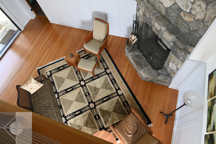 From the second story, looking over the balcony at this St. George, Maine great room with fieldstone fireplace
