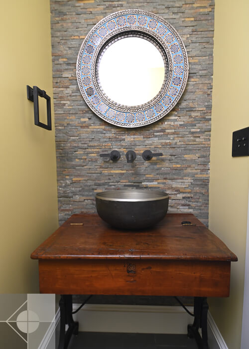 Custom bowl sink on wooden table with custom stone tile and mirror in this St. George, Maine home.