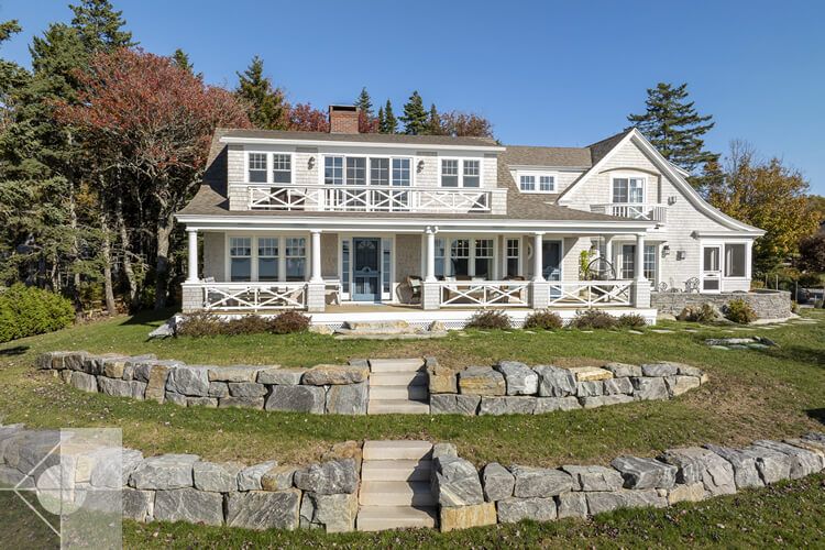 Drone view of the house, curved fieldstone wall and covered deck and porch.